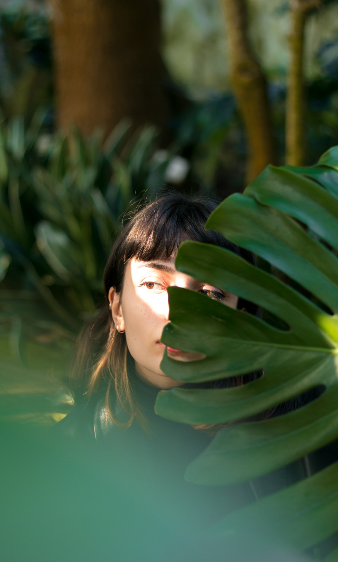  a woman hiding half her face behind a large leaf